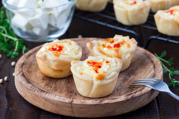 Feta cheese and fried onion mini quiche muffins, on wooden plate and cooling rack, horizontal, closeup