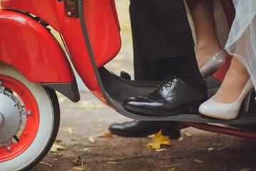 A unique cropped photo of groom and bride riding on the red motorbike in autumn time. Shoes of bride and groom on the scooter. Unforgettable wedding day with extreme riding