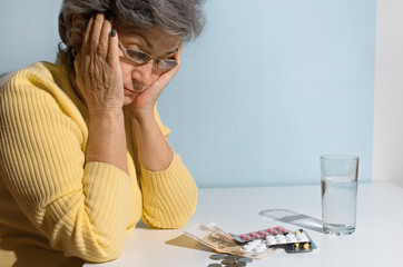 Fototapeta premium Elderly woman with glasses looking at money and pills on the table. Concept of depression, drug price, treatment cost