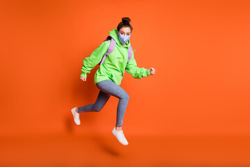 Fototapeta na wymiar Photo portrait full body view of running schoolgirl jumping up wearing blue fabric face mask isolated on vivid orange colored background