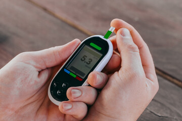 medicine, diabetes, glycemia, healthcare and people concept - man checking blood sugar with glucometer and test strip at home.