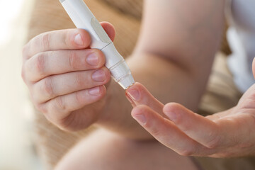 Medicine, diabetes, glycemia, healthcare and people concept - close up of a man's hands using a lancet on his finger to check blood glucose meter with copy space for text