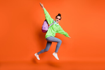 Full length photo portrait of schoolgirl making plane with hands jumping up isolated on vivid orange colored background