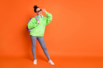 Fototapeta na wymiar Photo of cute young woman wear green hoodie schoolbag glasses looking empty space isolated vivid orange color background