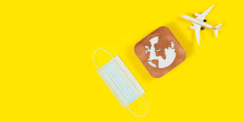 Plane model, face mask and earth model on a yellow background. Flight impact of coronavirus (COVID-19) concept.