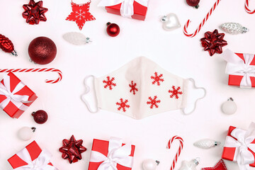 Festive face mask with snowflakes  surrounded by Christmas decorations and gifts on a white background.