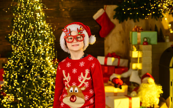 Kid wear santa hat and christmas sweater. Santa brought me gifts. December tradition. Sale discount. Real happiness. Child happy excited near christmas tree. Merry christmas. Happy childhood concept