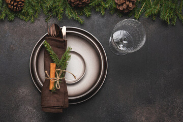 Simple Christmas place setting with plates , utensils and napkin decorated with spruce branch and cinnamon on brown table