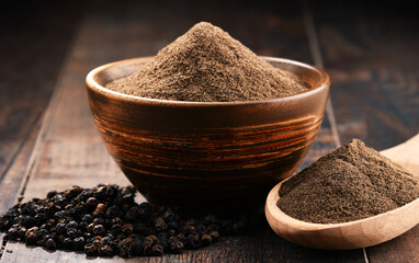 Composition with bowl of ground black pepper on wooden table