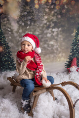 Sweet blond toddler child, playing on a sledge in the snow