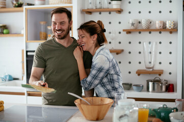Husband and wife making pancakes at home. Loving couple having fun while cooking..