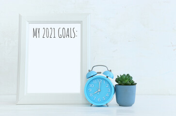 Business concept of top view 2021 goals list over frame, home plant over wooden desk