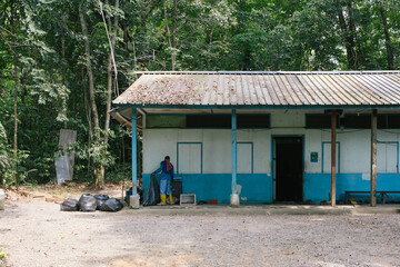 hut storage room blue structure building with rubbish bin bags in nature cleaner wearing boots tidying clearing up mess in jungle tall trees singapore