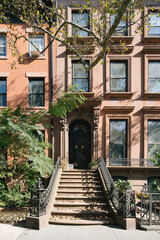 generic home facade in brooklyn new york city peach orange red walls black door blue reflective windows green trees stairs staircase shadows sunny residential