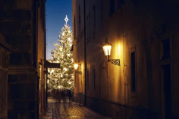 Rolgordijnen Narrow street Old Town against illuminated Christmas tree © Chalabala