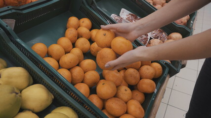 Young woman chooses tangerines at the market. Girl's hands close-up.