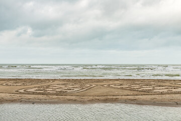 Koksijde, Belgium - November 21, 2020: Cloudy seaview with writing in the sand