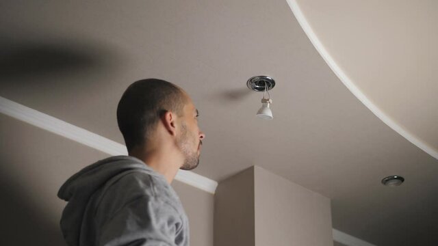 The process of replacing an LED lamp with a downlight. A man in the twilight repairs a ceiling soffit