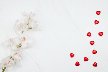 Valentine's white orchids with red chocolate hearts on a white marble background
