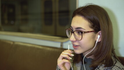 A young woman is talking on the phone through headphones in a subway train. Old subway car