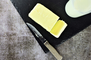 Block of butter, part of the milk bottle on slate board and old knife. Space for text or idea.