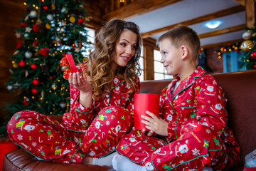 A young mother and son playing near the Christmas tree. Family in red Christmas pajamas. Christmas homeliness. Holidays and New Year's gifts
