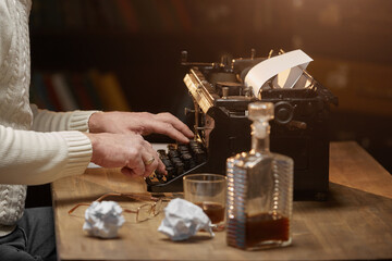 Close-up of men's hands typing on a typewriter, sitting at the home table against the background of the library