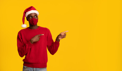 Fototapeta na wymiar Black Man In Protective Mask And Santa Hat Pointing At Copy Space