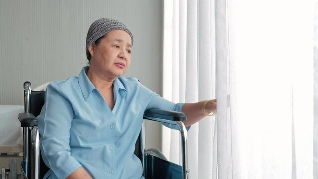 Senior patient Asian woman sitting in wheel chair in nusing home or hospital ward in front of window with curtain and thinking. Lonely elderly woman spending day alone at hospital. Oldness, disability