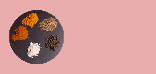 Various spices sea salt, black peppercorns, paprika, tumeric on round shale palette on pink background.  Copy space. Banner.