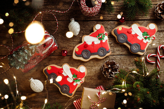 Christmas gingerbread cars, fir branches, red decorations, lights garland, gift boxes on wooden background. Merry Christmas and New Year holiday. Xmas cookies, top view, bokeh