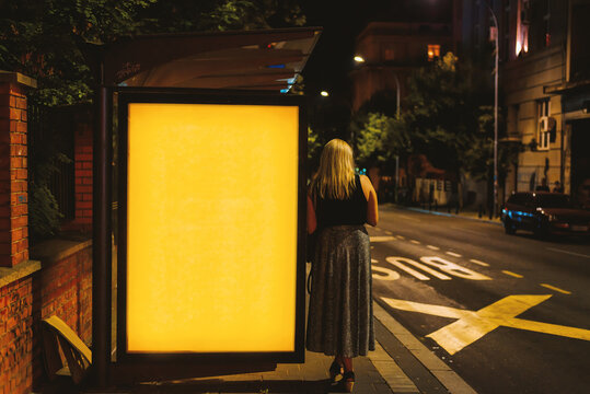 Illuminated blank billboard with copy space for your text message or content with woman standing by billboard