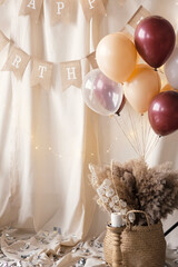 Boho style photo zone. Old wooden chair, hat, a garland of flags with the inscription Happy Birthday, a bouquet of pampas grass, candles, balloons.