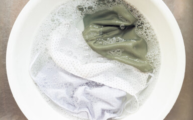 Eco-friendly Sustainable lifestyle, reduce medical single-use waste during Covid-19 pandemic. A few reusable cloth face mask soaking in water with antibacterial laundry detergent ready to hand wash.