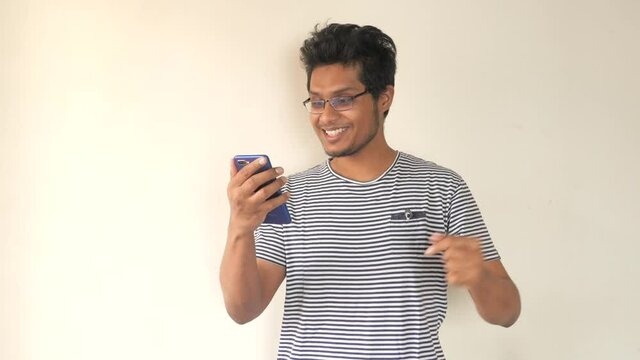 Smiling young man in glasses using his phone to make a video call, indoor 