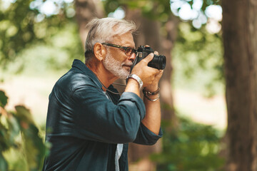 A gray-haired photographer with a beard takes pictures of nature while walking. Weekend hobby.