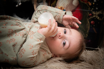 A little sleepy girl with a bottle of milk in her hand waiting for Santa Claus