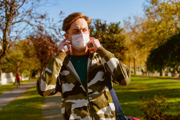 Young man going to the gym with his bag on his shoulder. wearing a protective mask is hiking through the woods. Young male athlete wearing a surgical mask is walking on the jogging track.