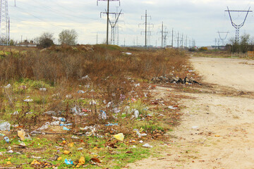 Heaps of rubbish on the side of the road. A line of high-voltage towers along the road. Ecology and environmental cleanliness theme. Third world country. Garbage on the sidelines