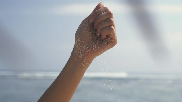 Time is running like sand through your fingers. Time, travel concept. woman hand sifting sand between fingers. unrecognisable lady enjoying paradise island near seaside in Bali, sun shine bright.