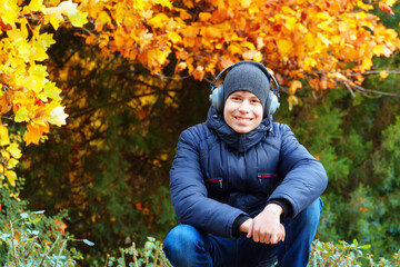 portrait of a teenager listening to music by headphones, relaxing in autumn city park, bright yellow maple leaves as background