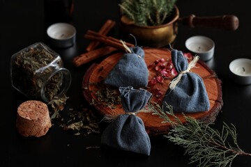 Yule winter solstice (Christmas) celebration themed magick spell bags made from blue cotton tied with yarn, filled with various herbs, spices. Dark black background with evergreens rose petals candles