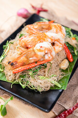 Shrimp, noodlesrice noodle and butter garlic fried shrimps sprinkled with pieces of chilli and chopped parsley on white dish on natural old wooden planks with spaghetti tongs, view from above, food
