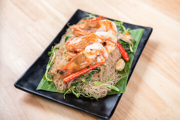 Shrimp, noodlesrice noodle and butter garlic fried shrimps sprinkled with pieces of chilli and chopped parsley on white dish on natural old wooden planks with spaghetti tongs, view from above, food
