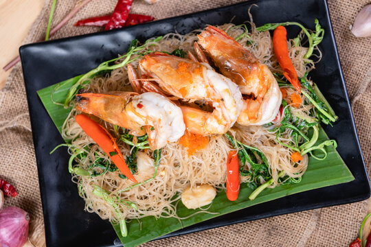 Shrimp, noodlesrice noodle and butter garlic fried shrimps sprinkled with pieces of chilli and chopped parsley on white dish on natural old wooden planks with spaghetti tongs, view from above, food