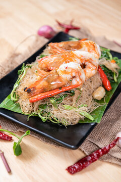 Shrimp, noodlesrice noodle and butter garlic fried shrimps sprinkled with pieces of chilli and chopped parsley on white dish on natural old wooden planks with spaghetti tongs, view from above, food
