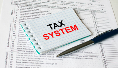 Notepad with text Tax System lying on financial tables with a pen