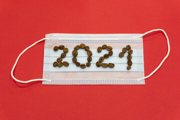 New Year 2021 and Merry Christmas. 2021 numbers from coffee beans on medical mask on red background