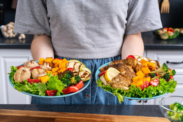 Woman holding plates with vegetables and fish cooked on home grill.