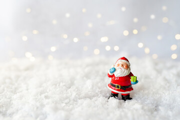 toy santa claus staying on the white snow, background with bokeh